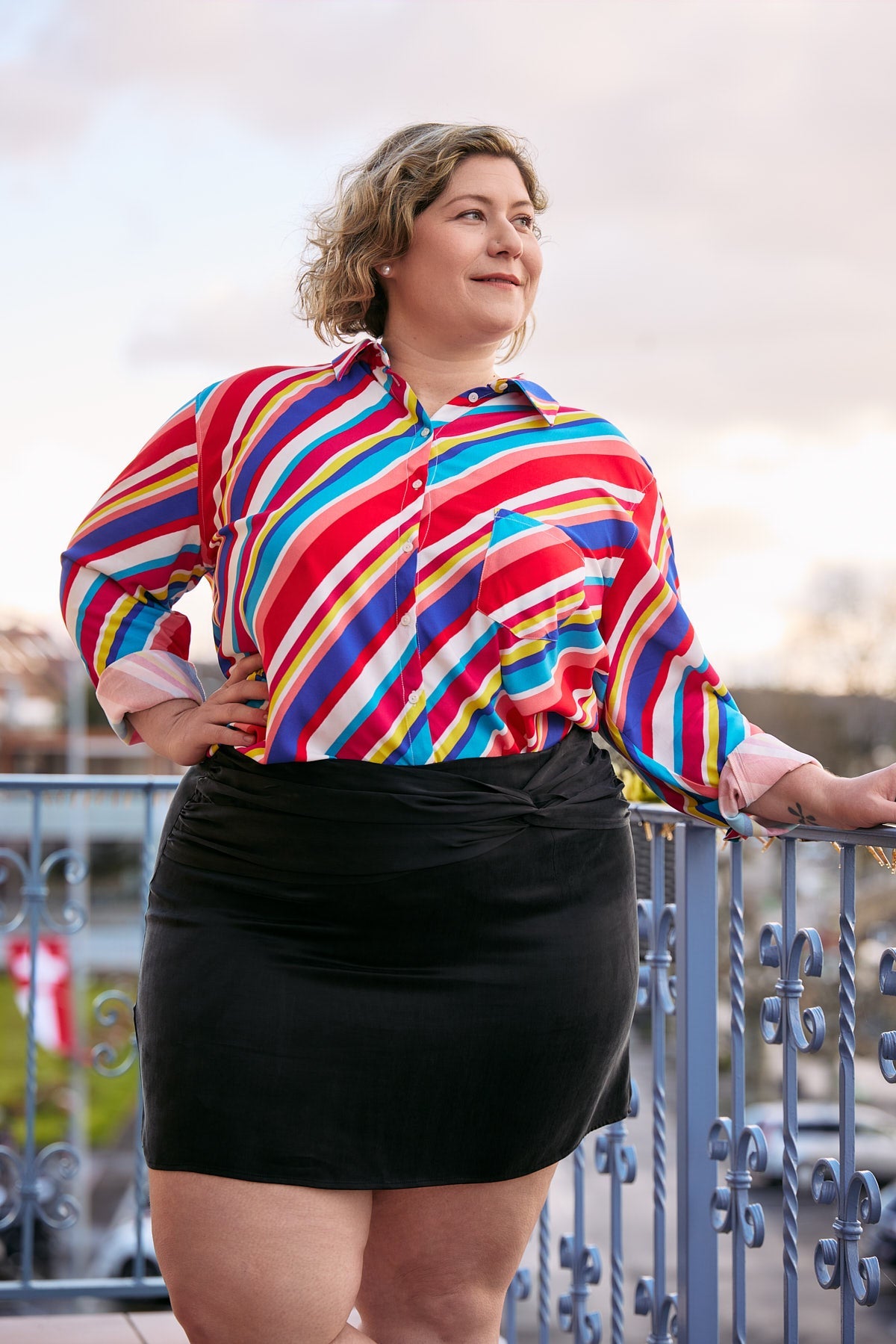 A curvy woman models the Katya Mini Skirt in black cupro, emphasizing its chic simplicity and figure-flattering design.