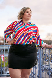 A curvy woman models the Katya Mini Skirt in black cupro, emphasizing its chic simplicity and figure-flattering design.