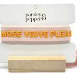 Close-up of adjustable salmon woven boho bracelet with offwhite border and orange embroidered “MORE VEUVE PLEASE” lettering, featuring sliding knot tassel cords.
