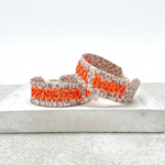Close-up of adjustable woven friendship bracelet with Leo pattern and neon orange embroidered "PROSECCO, BABY!" lettering with sliding knot cords.
