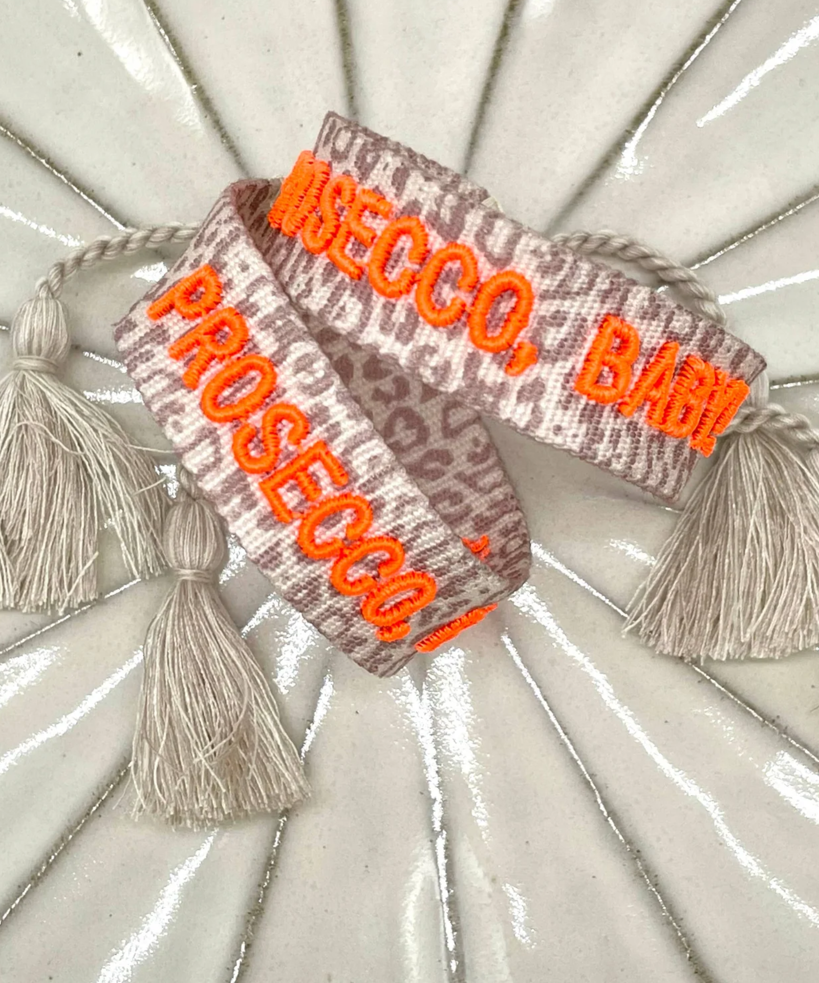 Close-up of adjustable woven friendship bracelet with Leo pattern and neon orange embroidered "PROSECCO, BABY!" lettering with sliding knot cords.