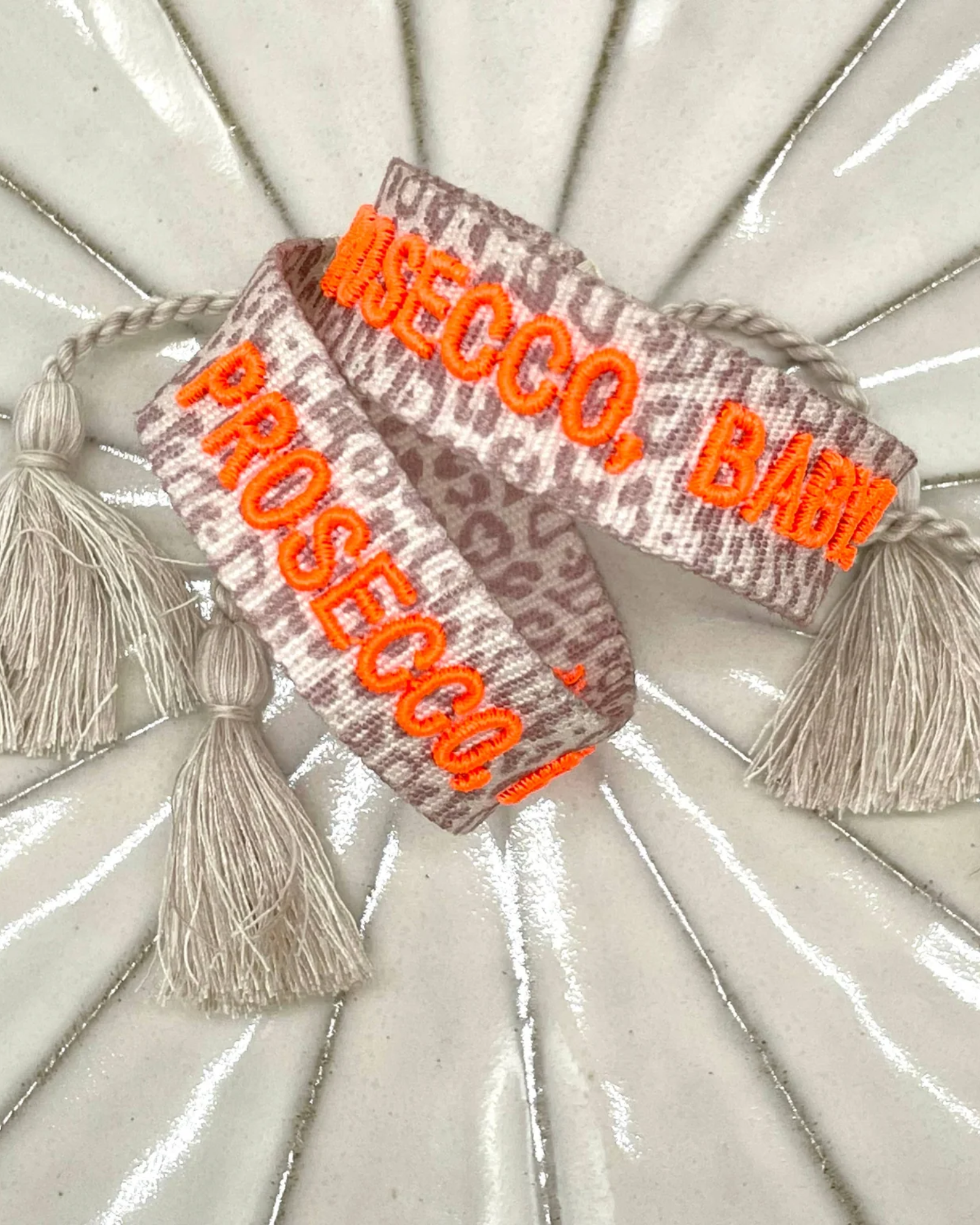 Close-up of adjustable woven friendship bracelet with Leo pattern and neon orange embroidered "PROSECCO, BABY!" lettering with sliding knot cords.