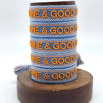 Close-up of adjustable blue and orange woven friendship bracelet featuring embroidered "SUNSHINE & GOOD VIBES" lettering and sliding knot tassel cords.