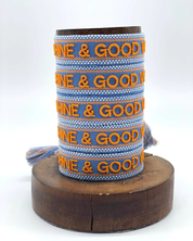 Close-up of adjustable blue and orange woven friendship bracelet featuring embroidered "SUNSHINE & GOOD VIBES" lettering and sliding knot tassel cords.
