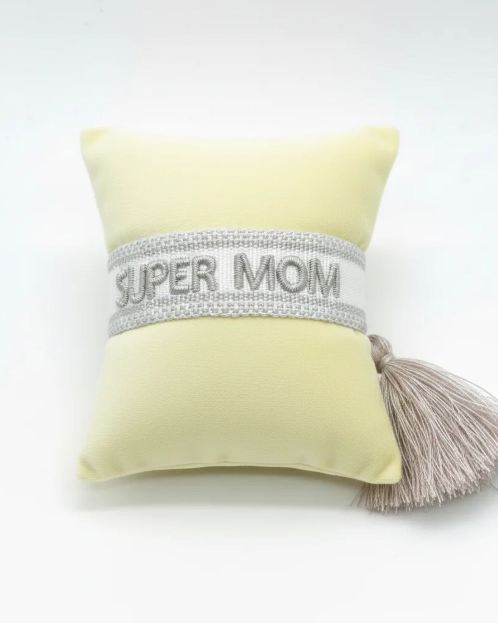 Close-up of adjustable white woven friendship bracelet with silver embroidered “SUPER MOM” lettering and sliding knot tassel cords.