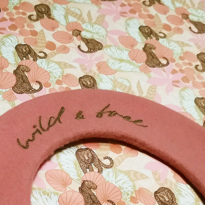 A close-up of the hand embroidered text "Wild & Free" and the lining of the Merino Wool Beret, featuring a super cute elastic lining for maximum comfort and flexibility.