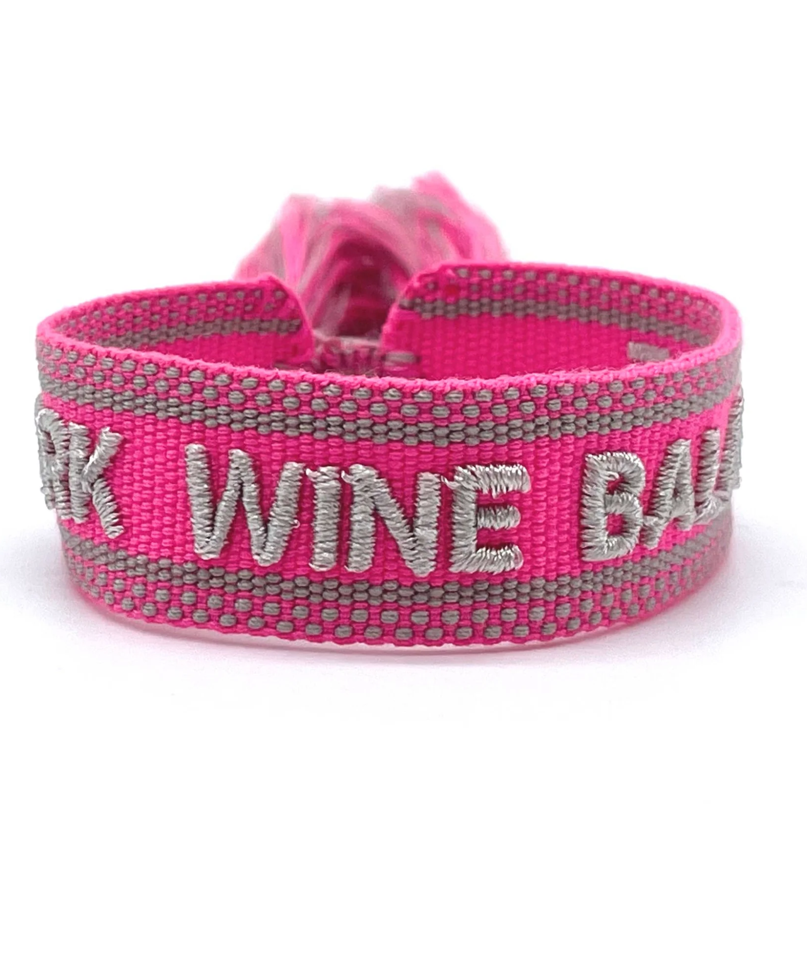Close-up of adjustable pink woven bracelet with silver gray embroidered “WORK WINE BALANCE” lettering, matching border, and sliding knot tassel cords.