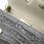 Model in a white outfit and straw hat with the Aetalia Ary evening bag in olive crocodile print