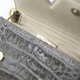 Model in a white outfit and straw hat with the Aetalia Ary evening bag in olive crocodile print