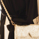 Aetalia Ary evening bag in silver crinkled leather worn on the shoulder with a black dress, gold chain strap