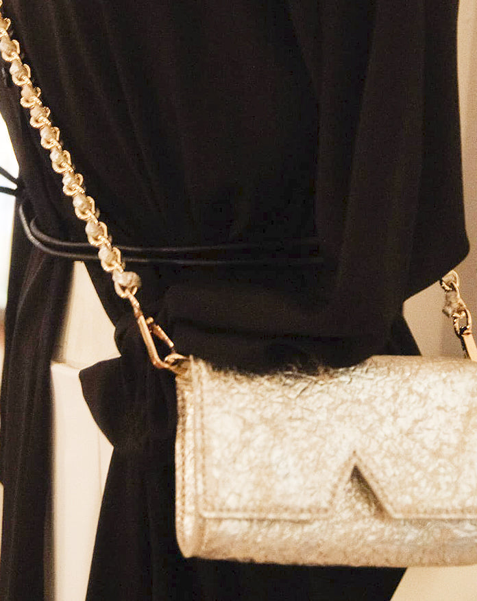 Aetalia Ary evening bag in silver crinkled leather worn on the shoulder with a black dress, gold chain strap