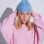 COLORUSH Byron beanie in Stonewash, hands on the beanie, with a pale pink jumper