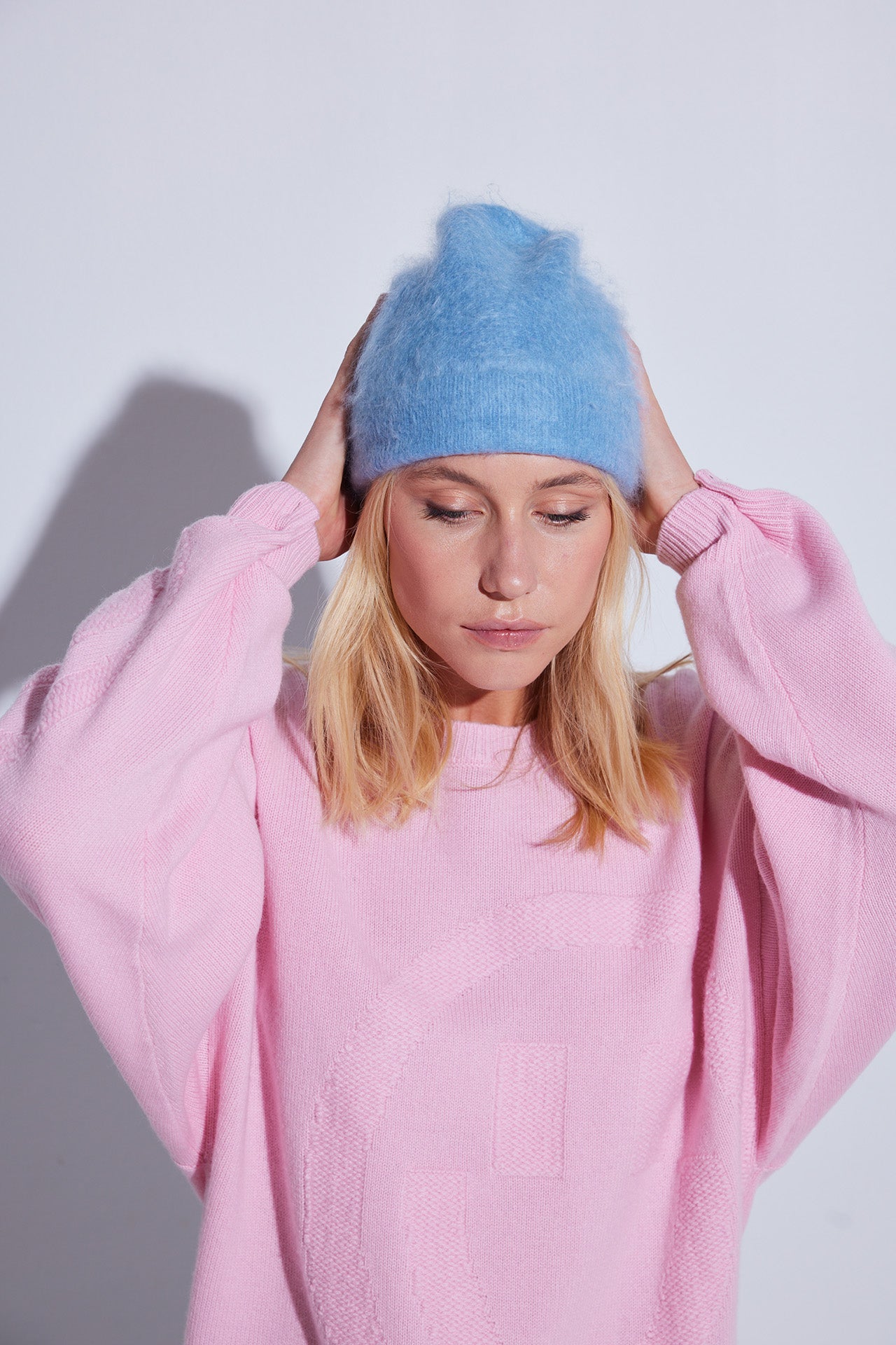 COLORUSH Byron beanie in Stonewash, hands on the beanie, with a pale pink jumper