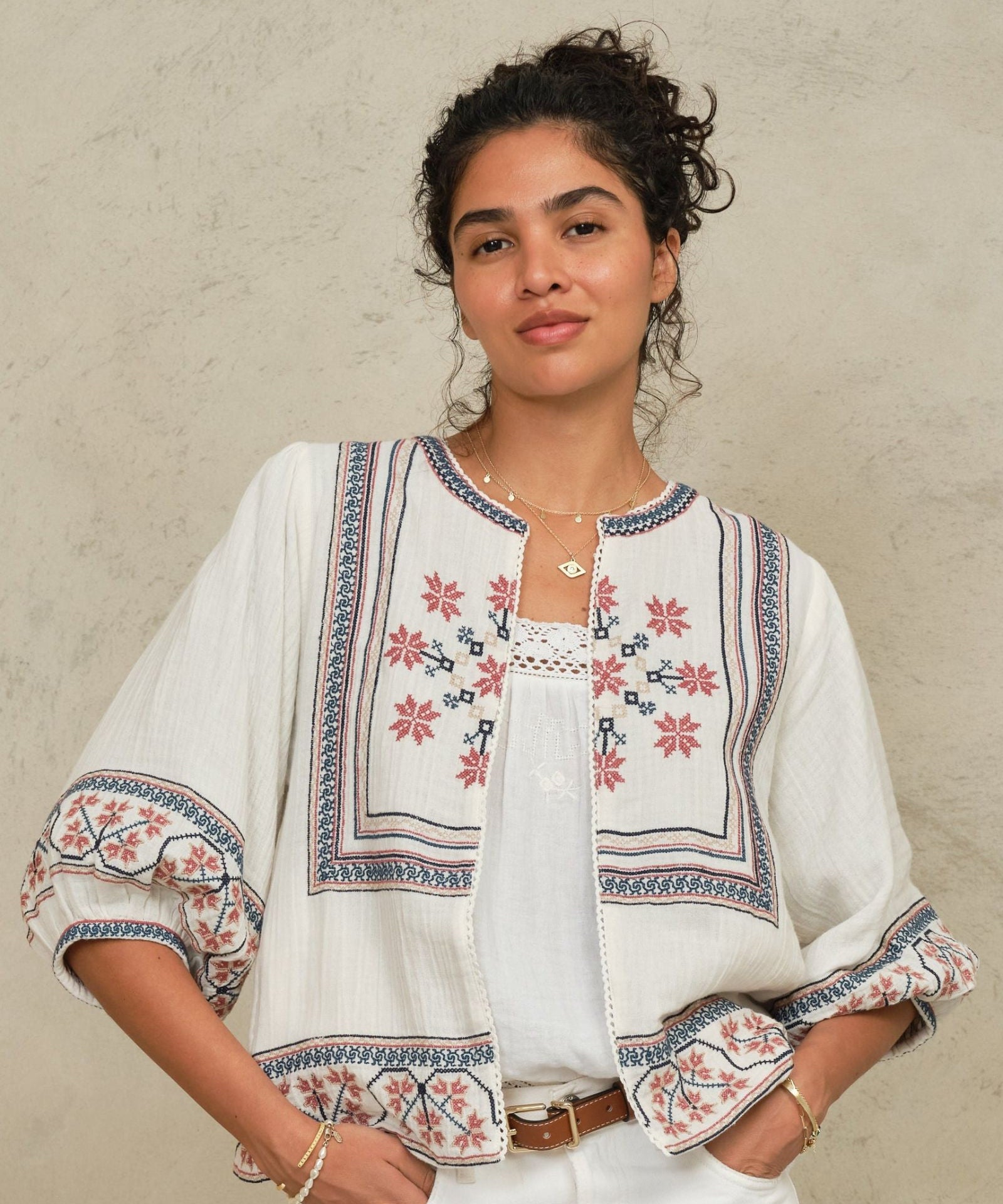 Model wearing an open-front Mabe Apparel embroidered cotton jacket with white trousers.