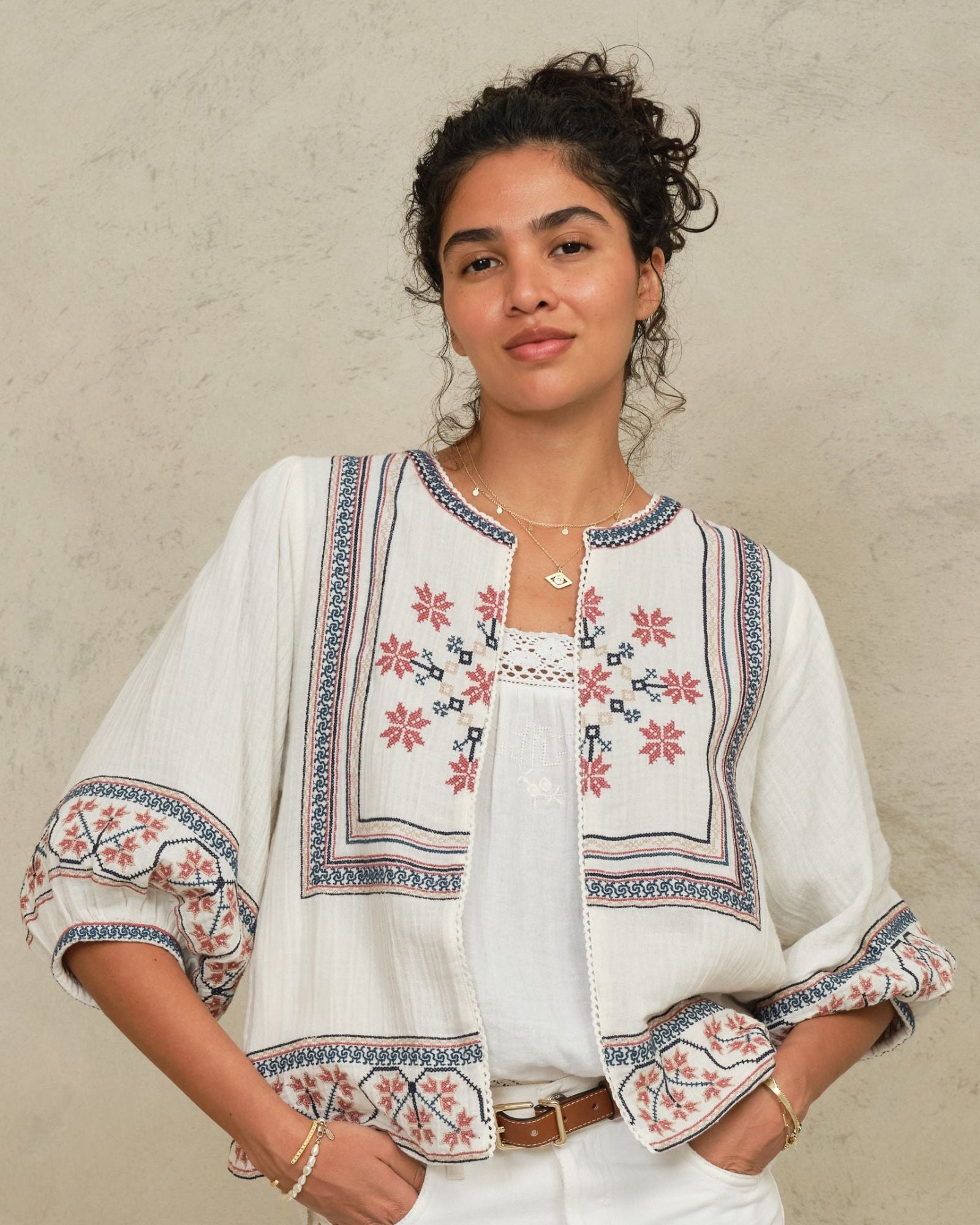 Model wearing an open-front Mabe Apparel embroidered cotton jacket with white trousers.