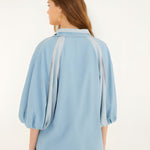 Rear studio view of the FARM Rio fluid denim blouse, highlighting the comfortable relaxed drape and voluminous puff sleeves.