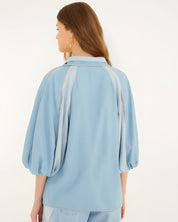 Rear studio view of the Farm Rio fluid denim blouse, highlighting the comfortable relaxed drape and voluminous puff sleeves.