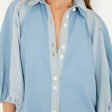 Close-up view of the FARM Rio bicolor blue denim blouse, focusing on the soft collar, distinct white crochet buttons, and open-knit lace inserts at the shoulders.