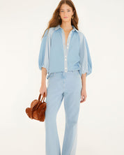Full-length studio shot of a model styling the Farm Rio bicolor blue denim blouse with matching denim pants, holding a textured brown handbag.