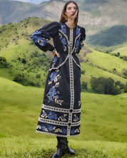 Full-length outdoor lifestyle view of a model in the Farm Rio Black Bold Flowers midi dress, paired with boots in a scenic green landscape.