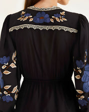 Close-up view of the Farm Rio Black Bold Flowers midi dress from behind, highlighting the intricate blue floral embroidery and geometric lace trim on the upper back yoke.