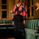 Lifestyle look view of a model in a restaurant setting wearing the FARM Rio Black Midnight Leopards jacquard maxi skirt paired with a floral cardigan.