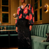 Lifestyle look view of a model in a restaurant setting wearing the FARM Rio Black Midnight Leopards jacquard maxi skirt paired with a floral cardigan.