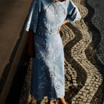 Full-length outdoor shot of a model wearing the Farm Rio denim Richelieu embroidered midi skirt on a patterned stone walkway.
