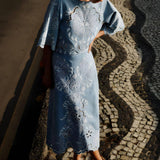Full-length outdoor shot of a model wearing the Farm Rio denim Richelieu embroidered midi skirt on a patterned stone walkway.