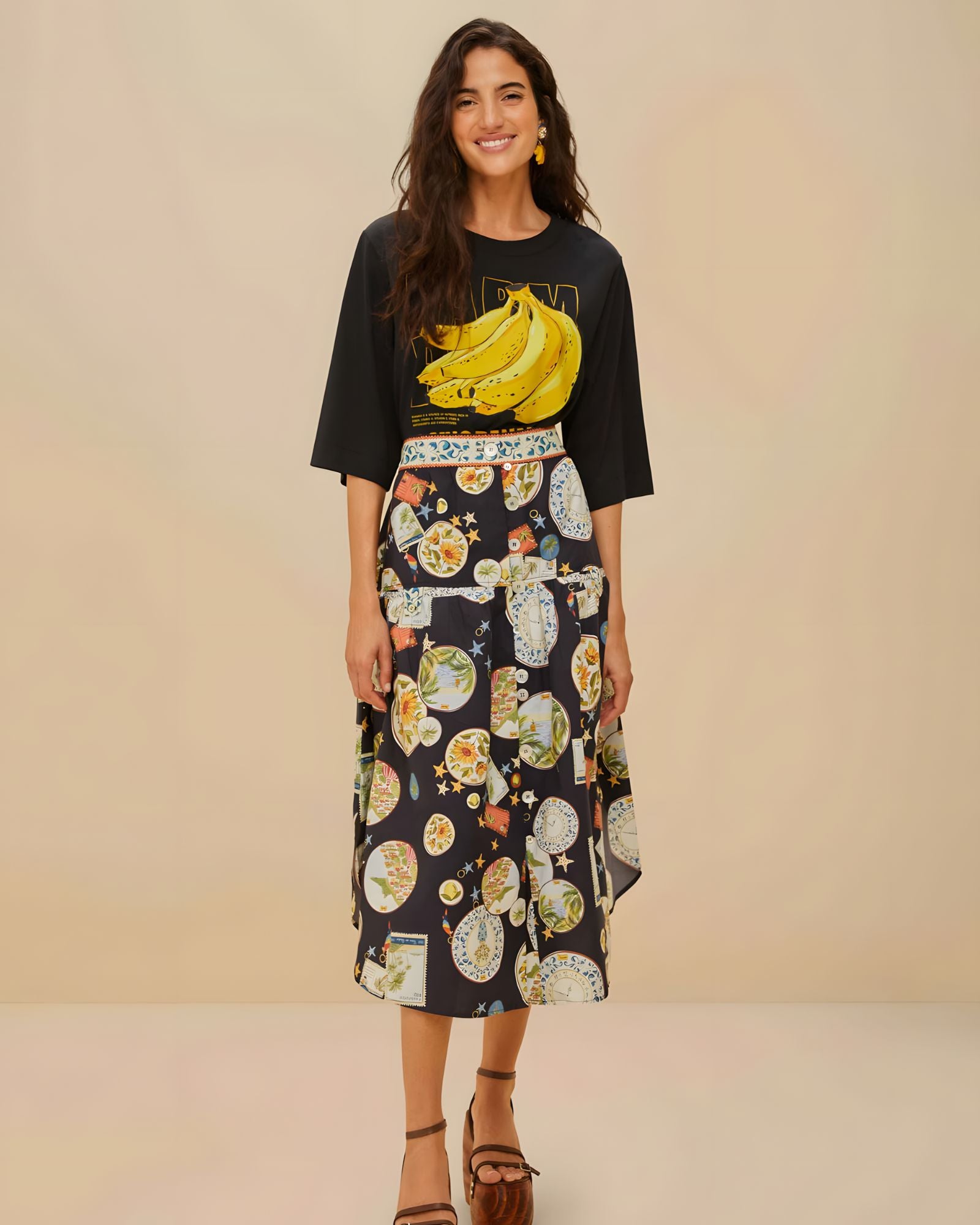 Full body view of a model styling the black Farm Rio graphic t-shirt with a patterned midi skirt