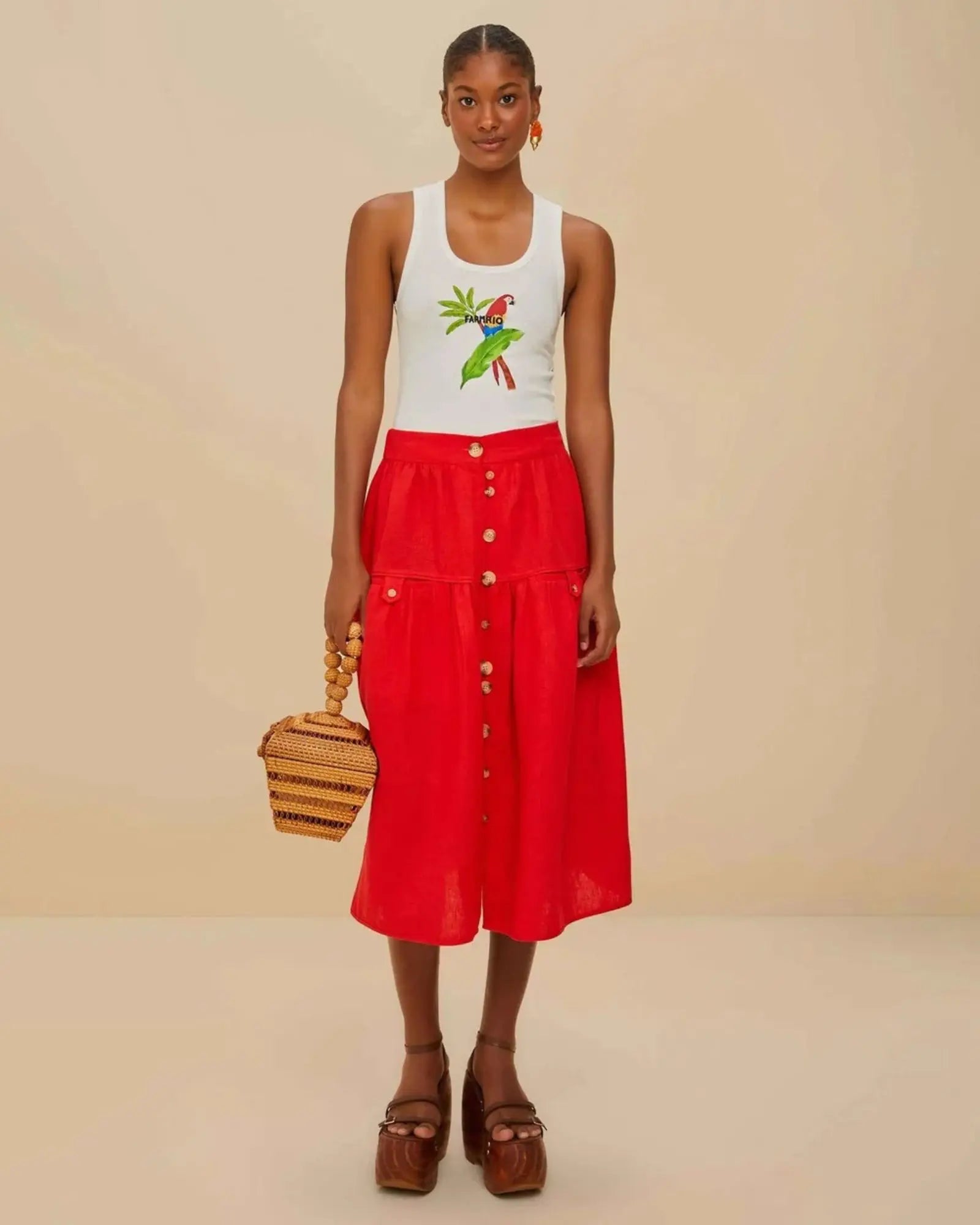 Woman wearing  white tank top with a parrot design by Farm Rio styled wth the Farm Rio red midi skirt .