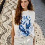 Front street style view of a model wearing the Farm Rio Off-White Toucan Rio padded shoulder t-shirt on a mosaic stone pavement.