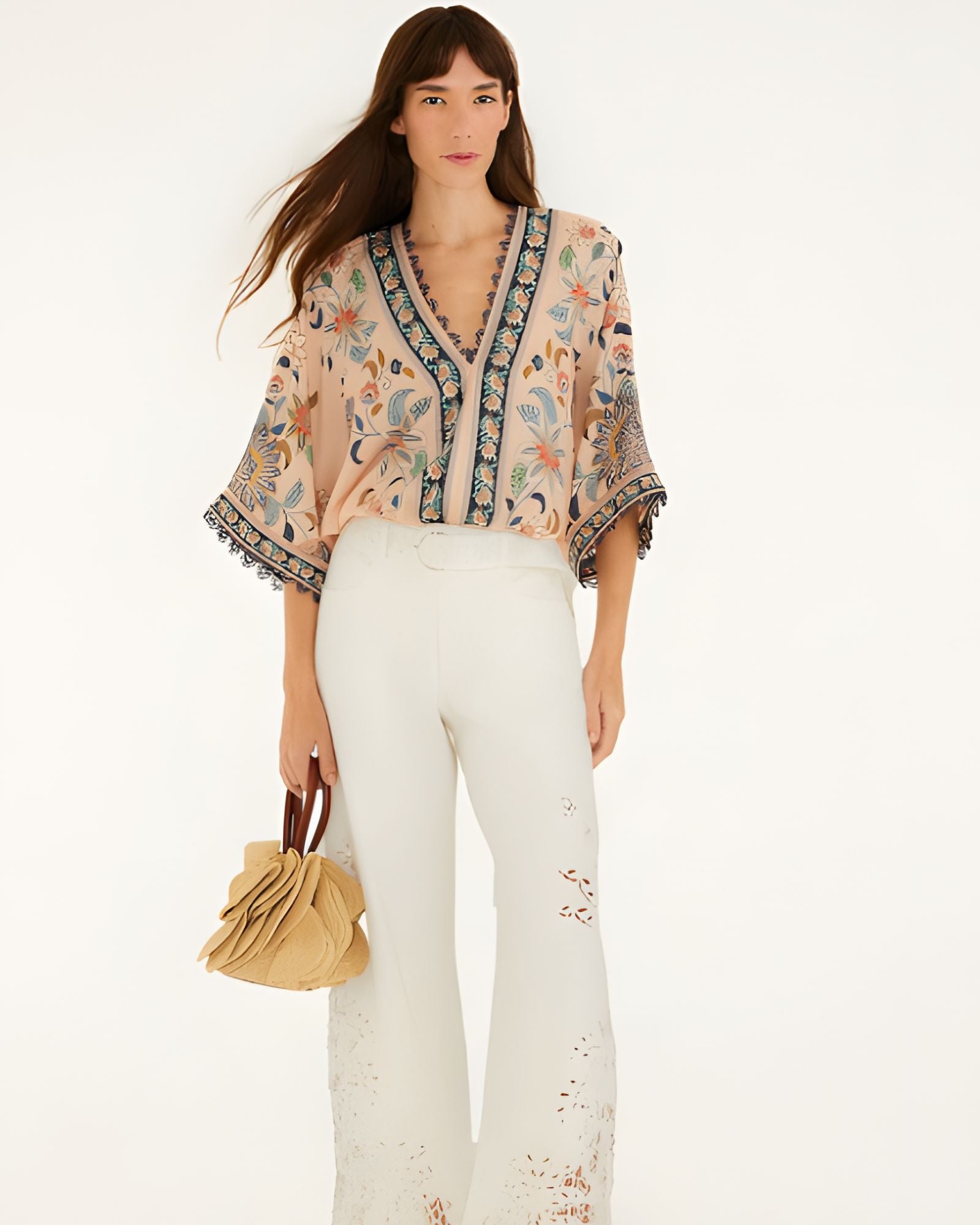 Model wearing Farm Rio soft pink floral delhi tapestry bodysuit paired with white trousers, full length view.