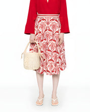 Full-length front view of a model styling the Farm Rio A-line midi skirt with a red top, neutral sandals, and a woven bucket bag.