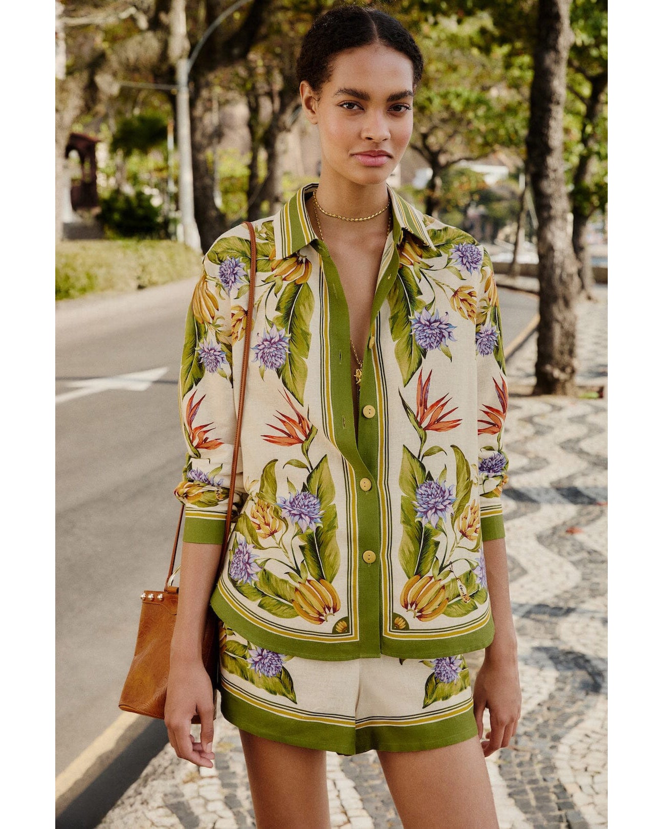 Woman wearing a patterned shirt and shorts standing on a street with trees in the background