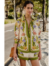 Woman wearing a patterned shirt and shorts standing on a street with trees in the background