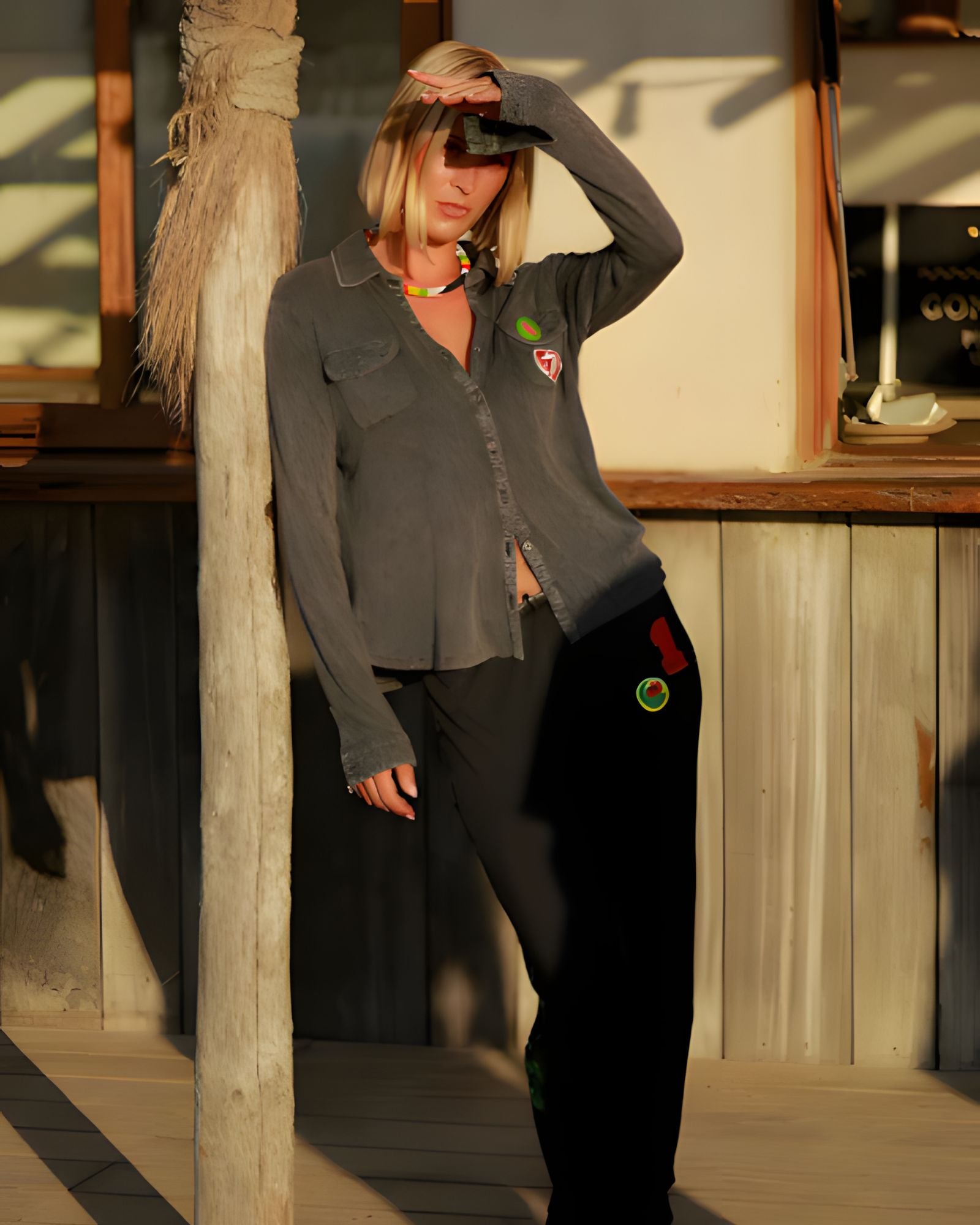 A model leaning against a wooden post outdoors, showcasing the casual streetwear aesthetic and comfortable drape of the charcoal Giulia sweatpants.