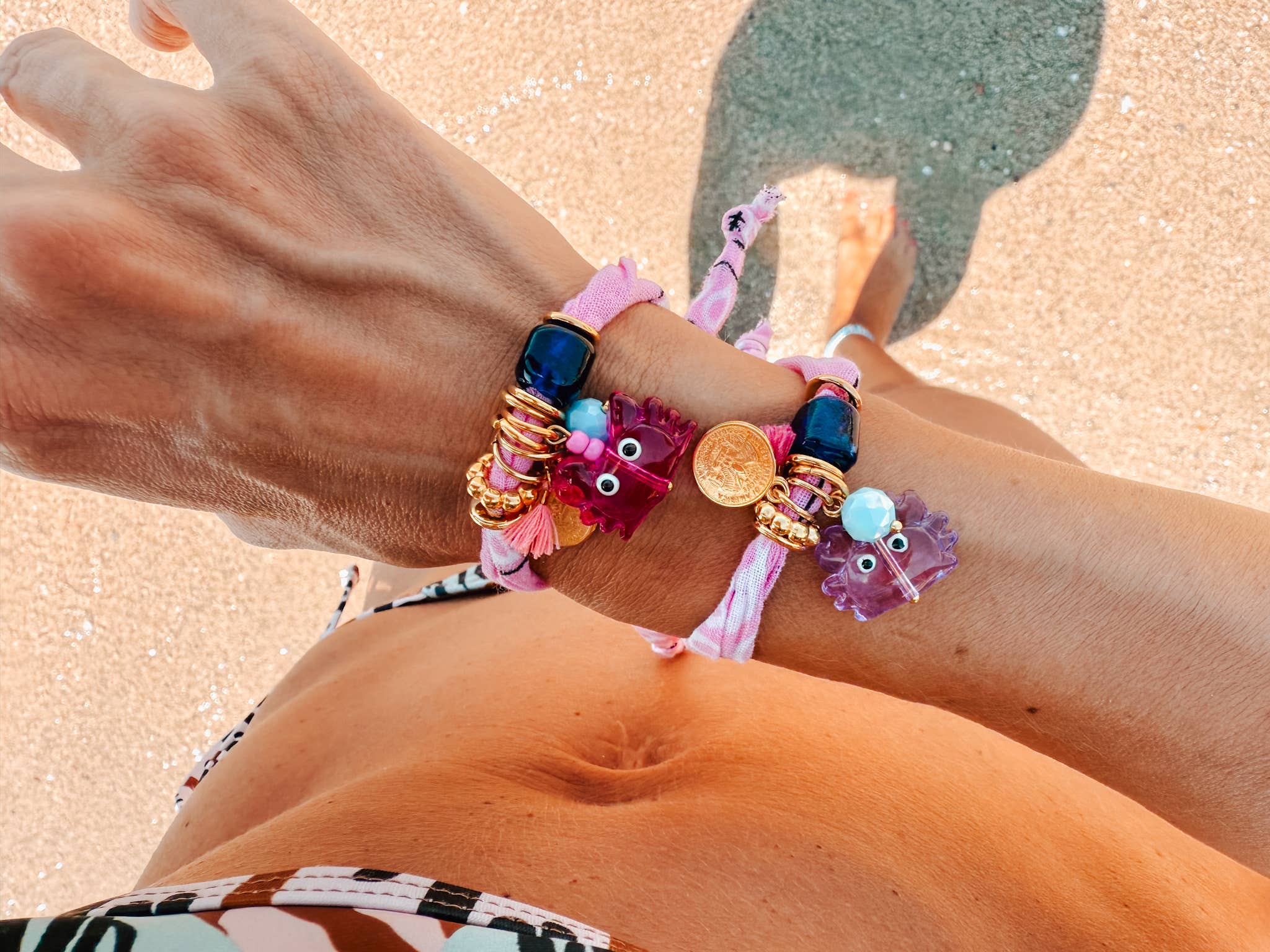 Close-up of a person's wrist two GOUPI bandana wrap bracelets, eaturing the fuchsia and lilac glass crab charms with 24k gold-plated accents
