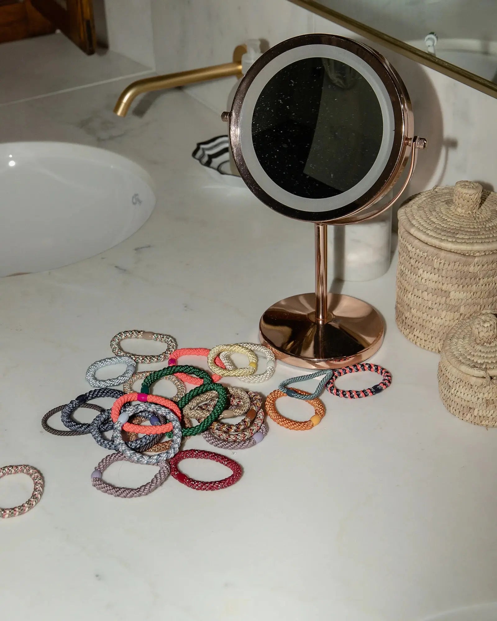 Colourful Kknekki hair elastics on a bathroom counter next to a makeup mirror