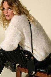Lifestyle shot of the black Nathan vegan leather strap worn crossbody with a white knit sweater