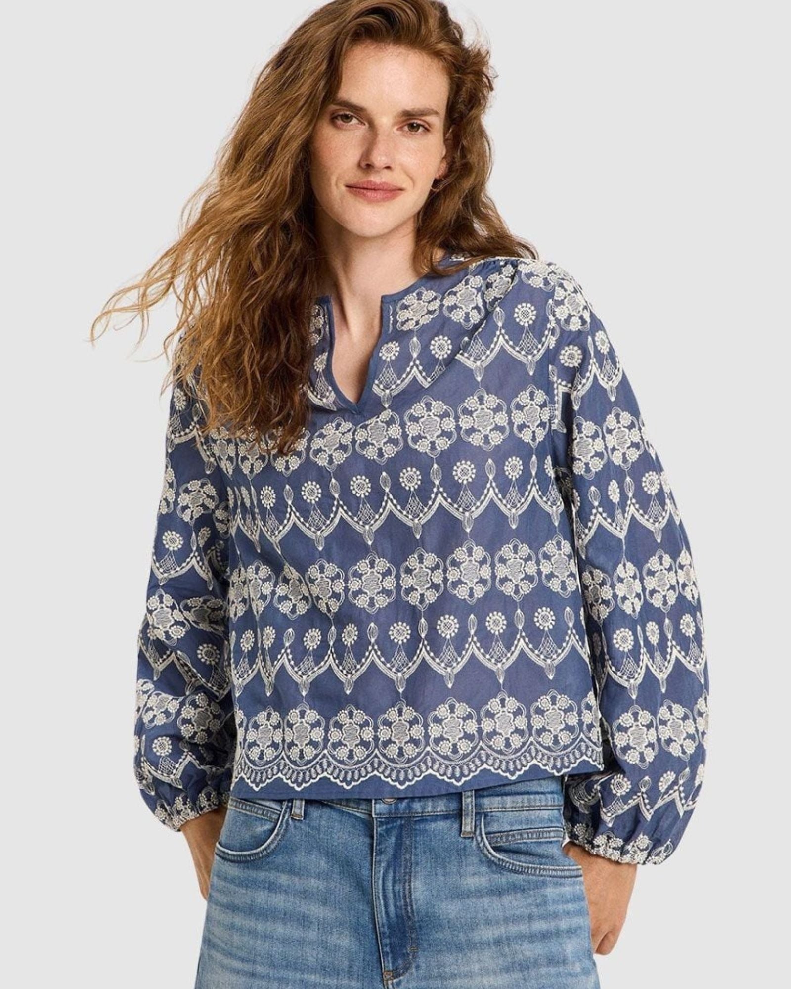 Lanius blue cotton blouse on a female model with long, wavy brown hair, showing the relaxed fit, V-slit neckline, and detailed white embroidery.