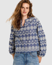 Lanius blue cotton blouse on a female model with long, wavy brown hair, showing the relaxed fit, V-slit neckline, and detailed white embroidery.