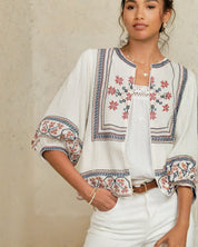 Close-up view of the red and blue geometric floral embroidery on a white Mabe Apparel cotton jacket.
