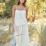 Woman in a Mabe Apparel cream cotton maxi skirt and matching camisole holding a woven bag outdoors.