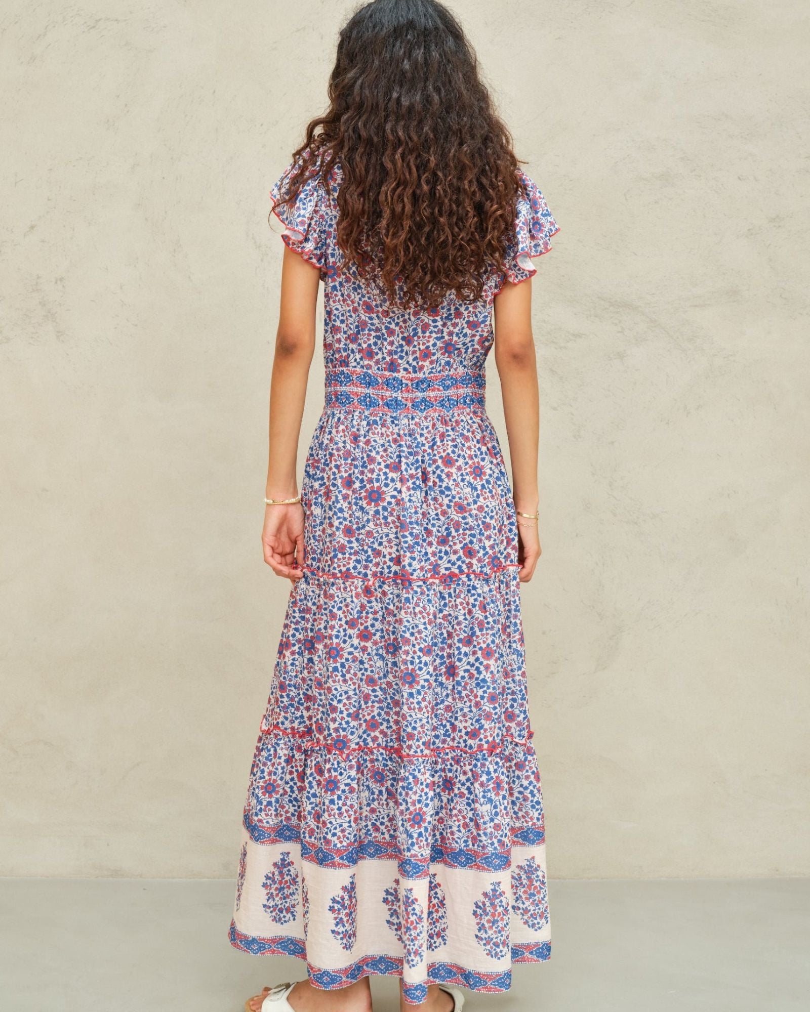 Back view of the tiered Mabe Apparel Della maxi dress in blue and pink artisan print on a model.