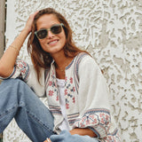 Model outdoors in sunglasses wearing a Mabe Apparel ecru embroidered cotton jacket with blue jeans.
