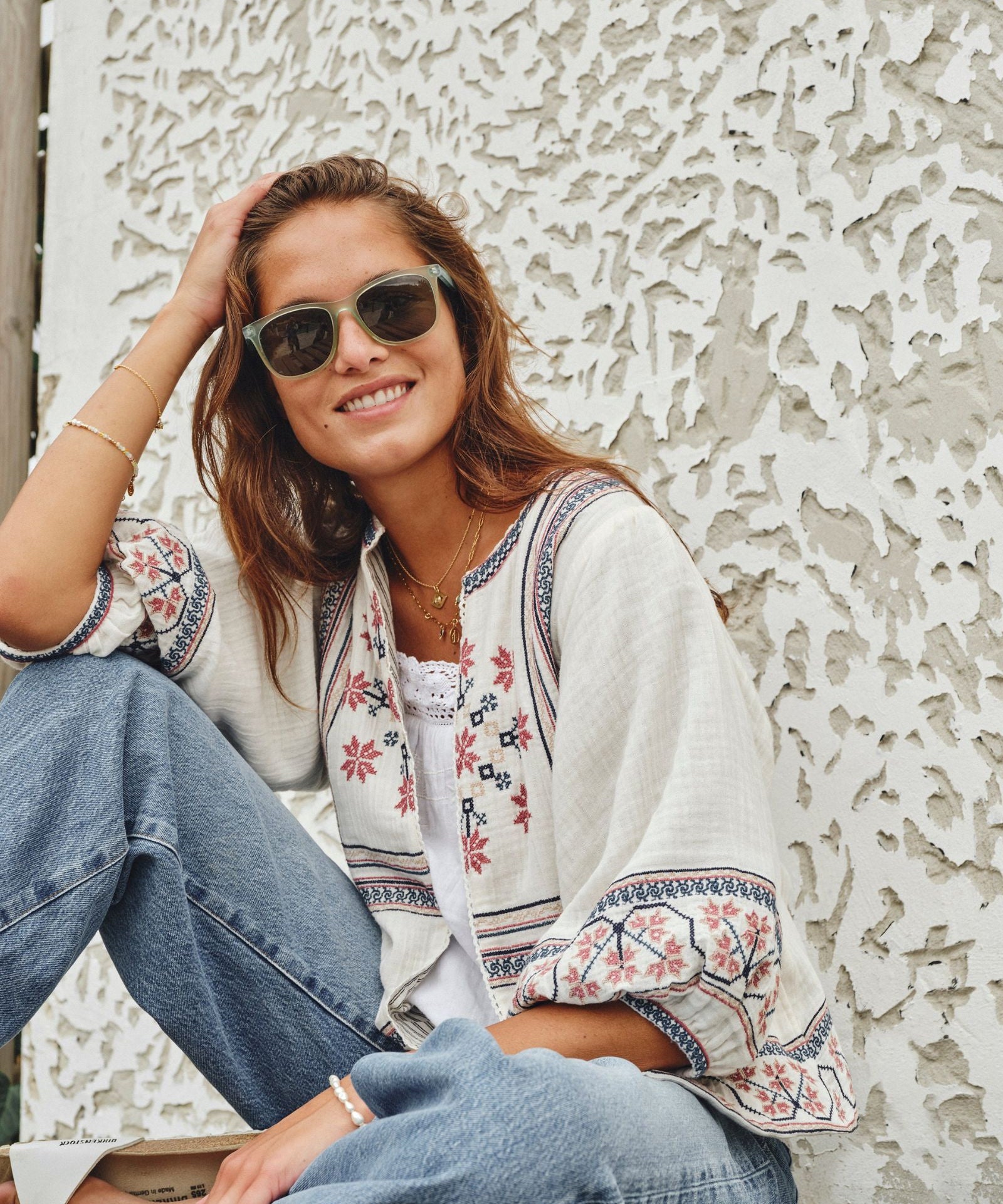 Model outdoors in sunglasses wearing a Mabe Apparel ecru embroidered cotton jacket with blue jeans.