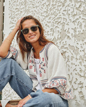Model outdoors in sunglasses wearing a Mabe Apparel ecru embroidered cotton jacket with blue jeans.