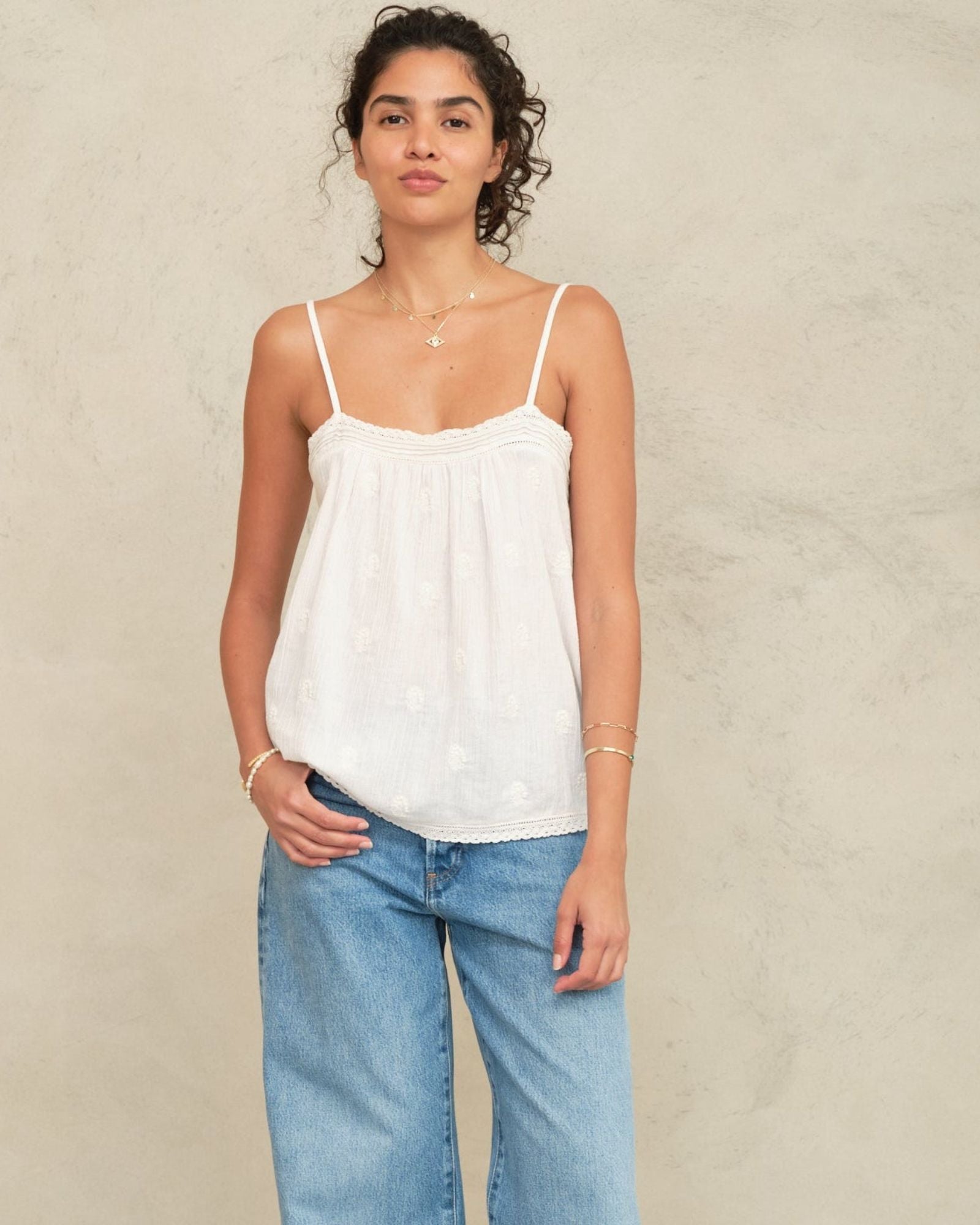 Woman wearing a Mabe Apparel white embroidered cotton camisole with blue jeans.