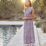 Woman in a Mabe Apparel Della resort maxi dress in blue and pink floral print with flutter sleeves.